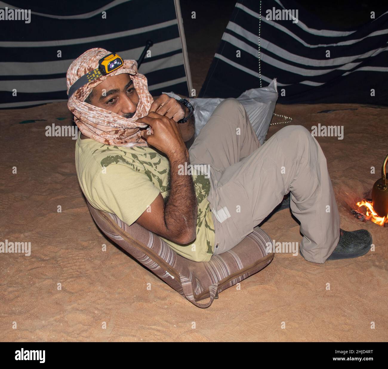 An Arabian man sits on a chair in the desert next to a campfire Stock Photo