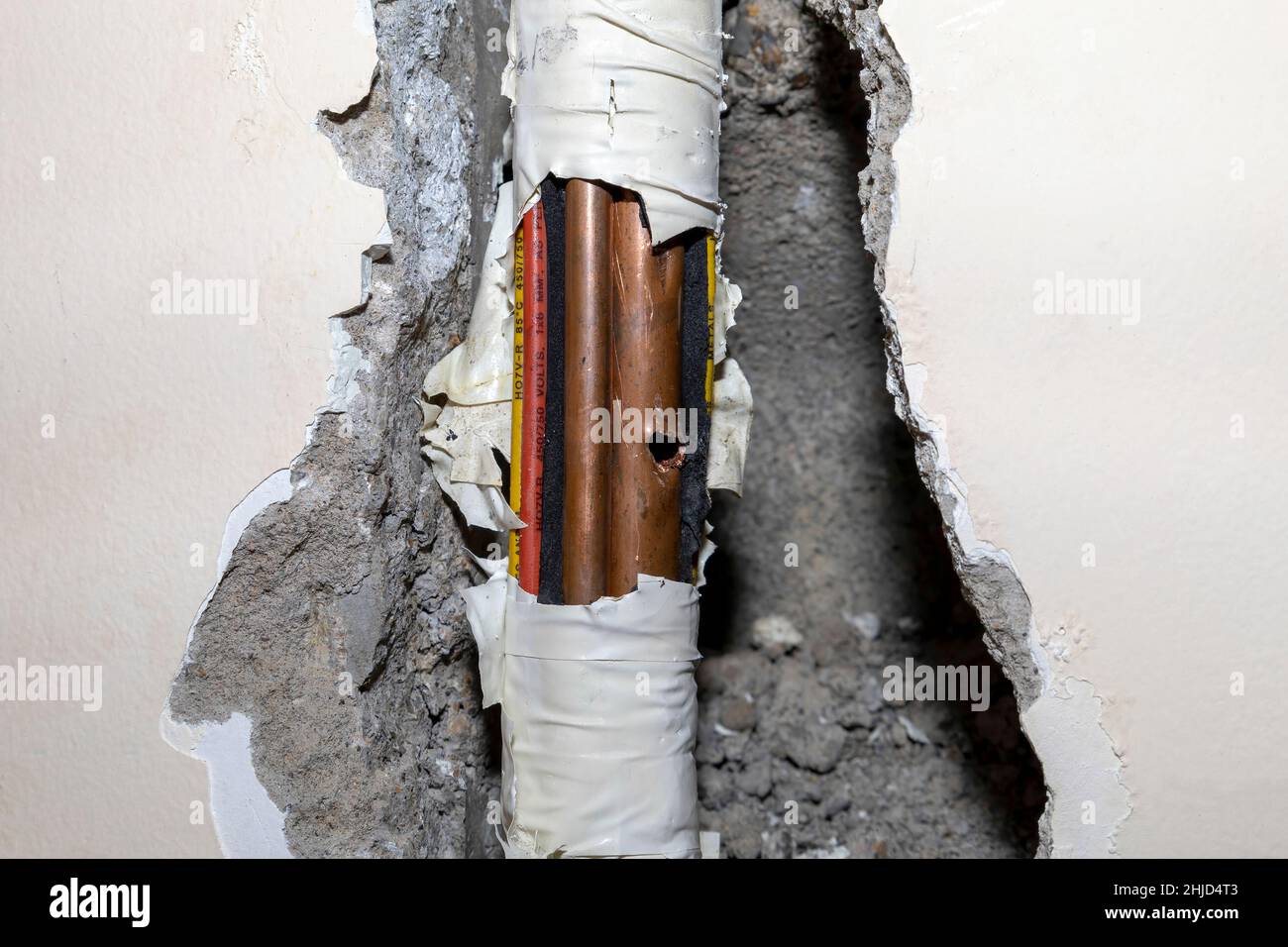 Damaged copper pipe in a wall surrounded by various wires and pipes Stock Photo Alamy