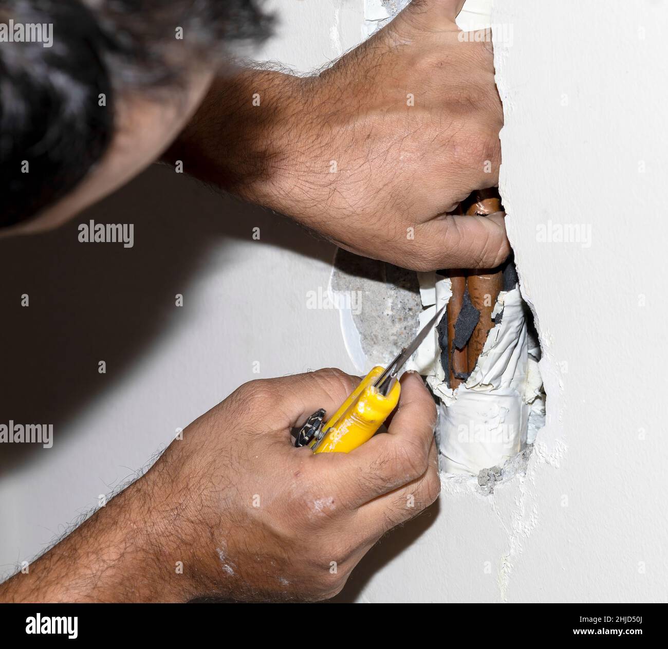 A repairman fixes a damaged copper pipe in the wall surrounded by
