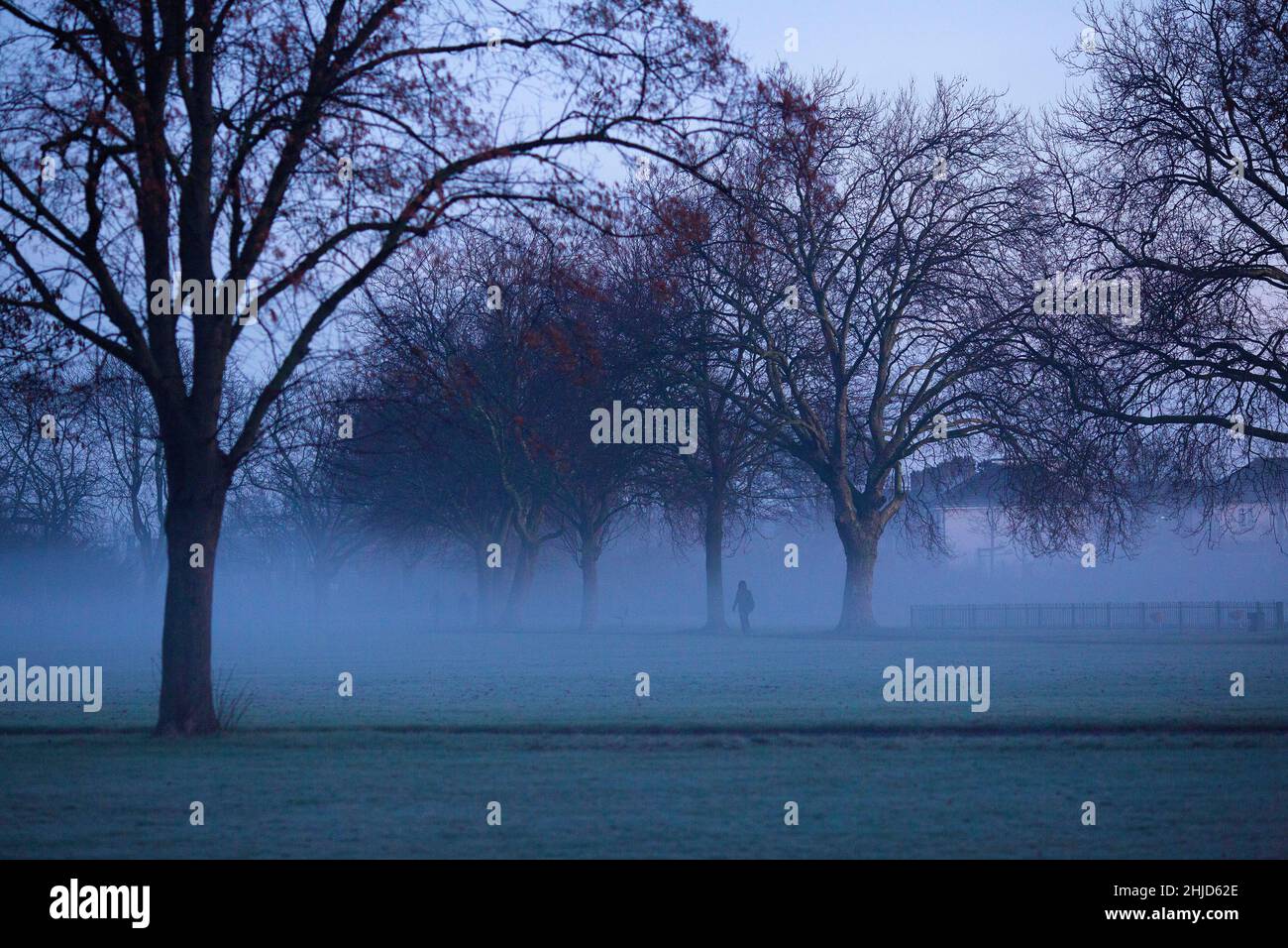 Pedestrians walk in a mist-covered park in Ilford, East London, in the morning. Stock Photo