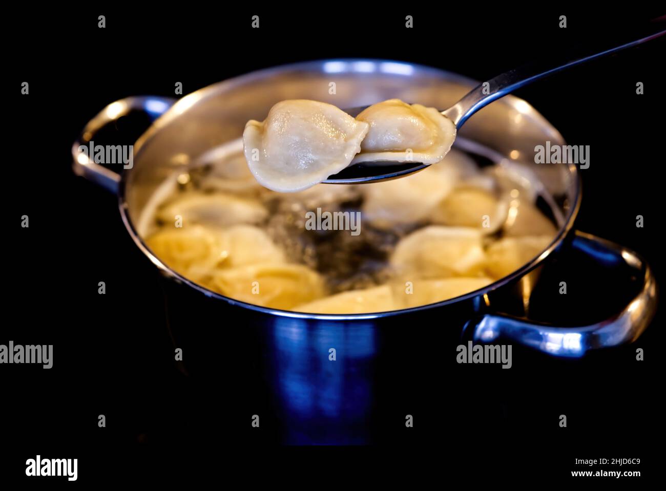 Dumplings mixed with a spoon in a pot of boiling water. Boiled dumplings in a pan. black background Stock Photo