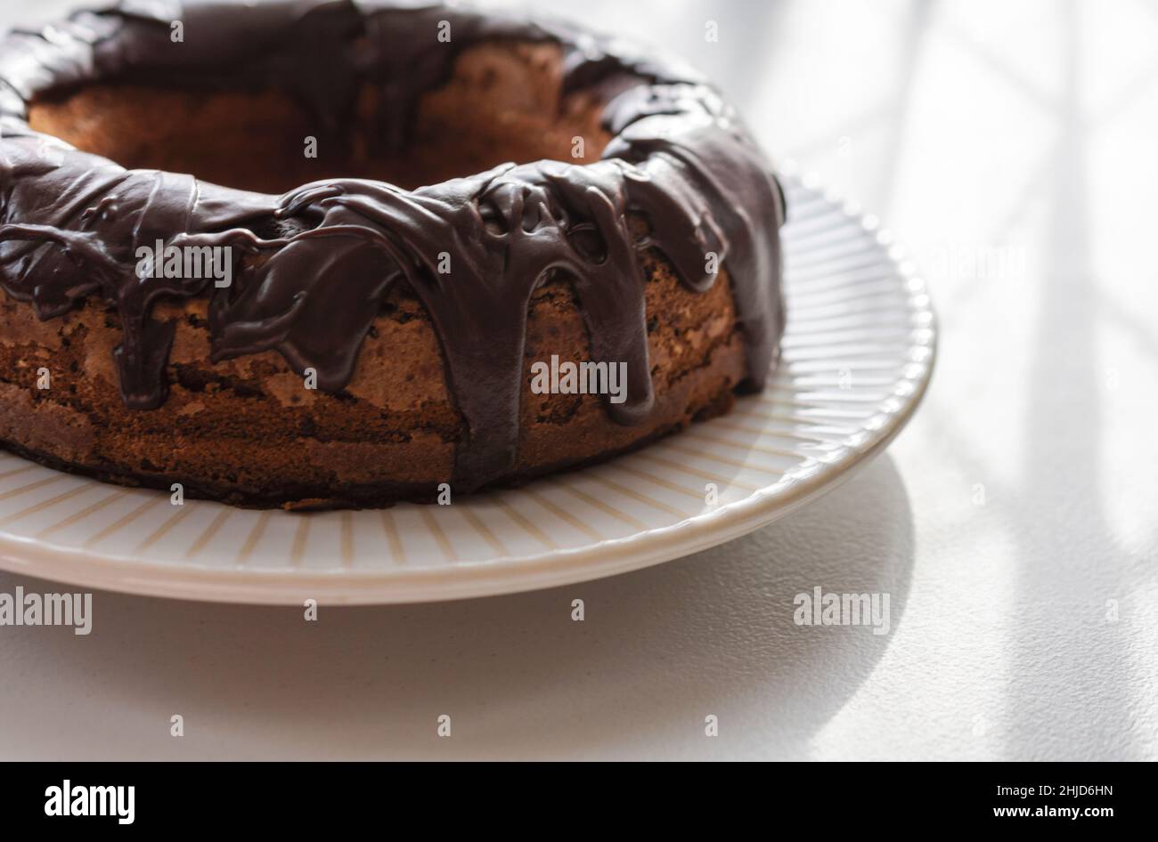 A whole chocolate bundt cake with fudge glaze.  Backlight from natural window light off camera. Stock Photo
