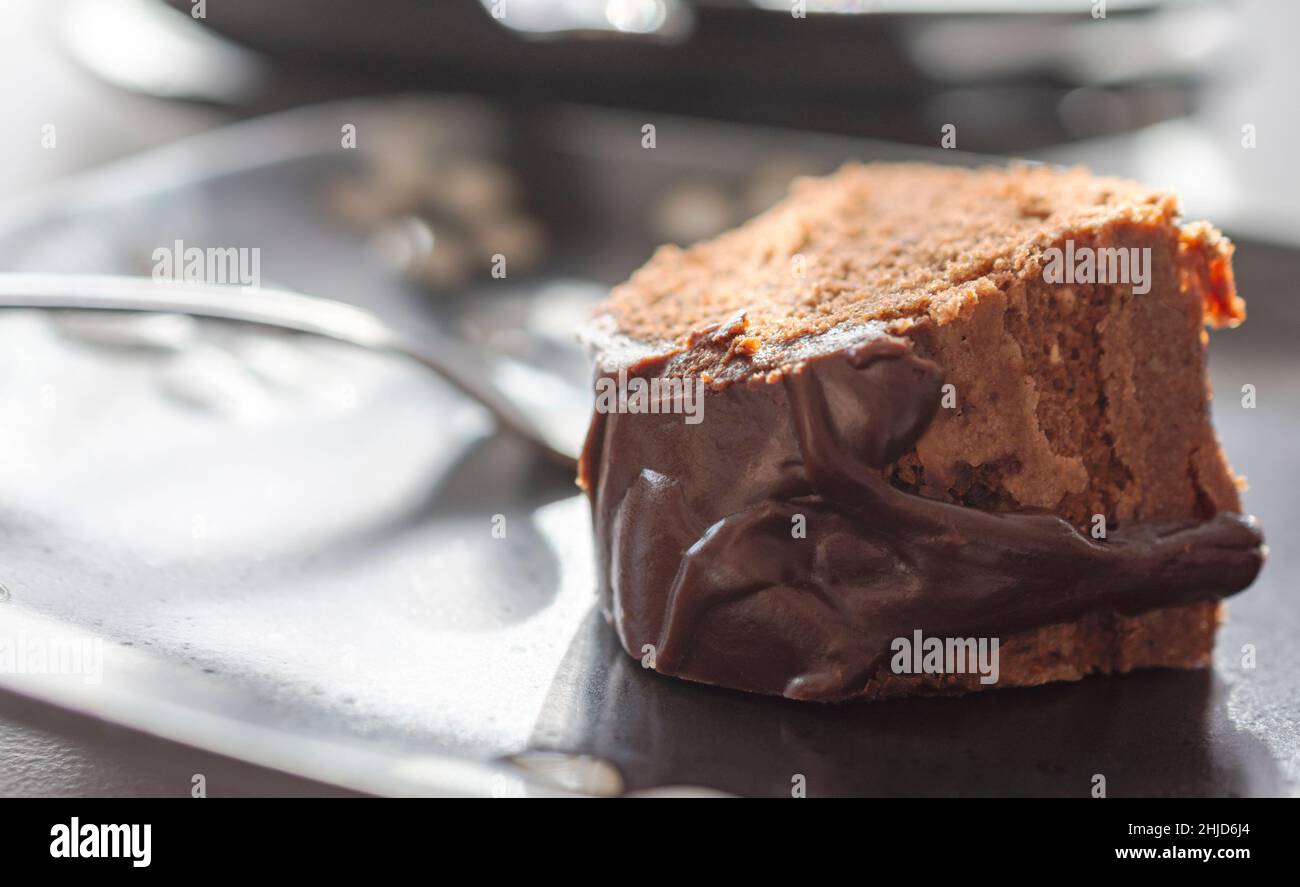 A slice of a chocolate bundt cake with fudge glaze on a black plate.  Fork blurred in background. Stock Photo