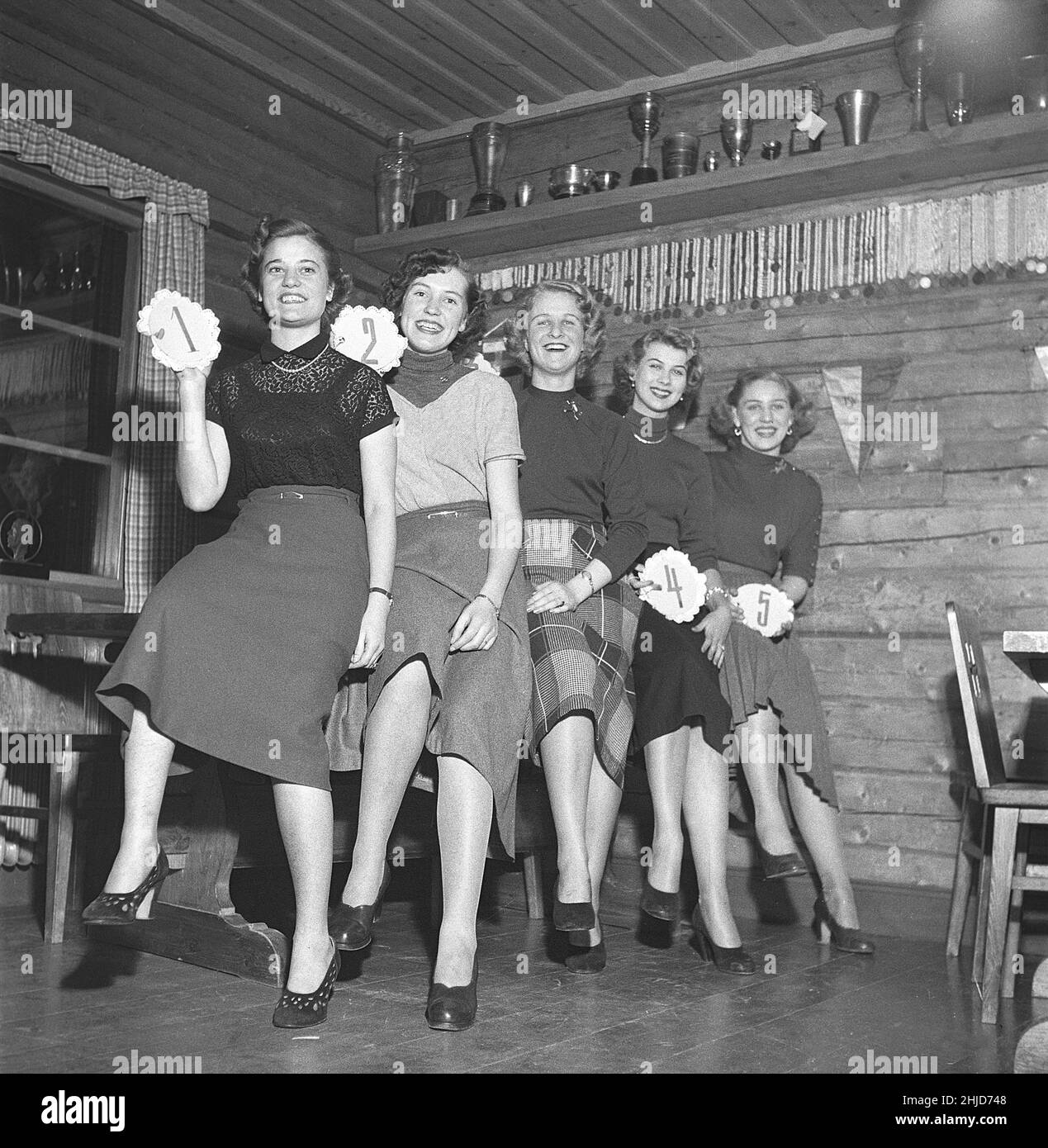 Women of the 1950s. Five young women each one holding a number from one to five. It's a rustic environment with timber walls. A beauty contest of some sort but the names of the girls are unknown. Sweden 1951 Kristoffersson ref BE66-7 Stock Photo