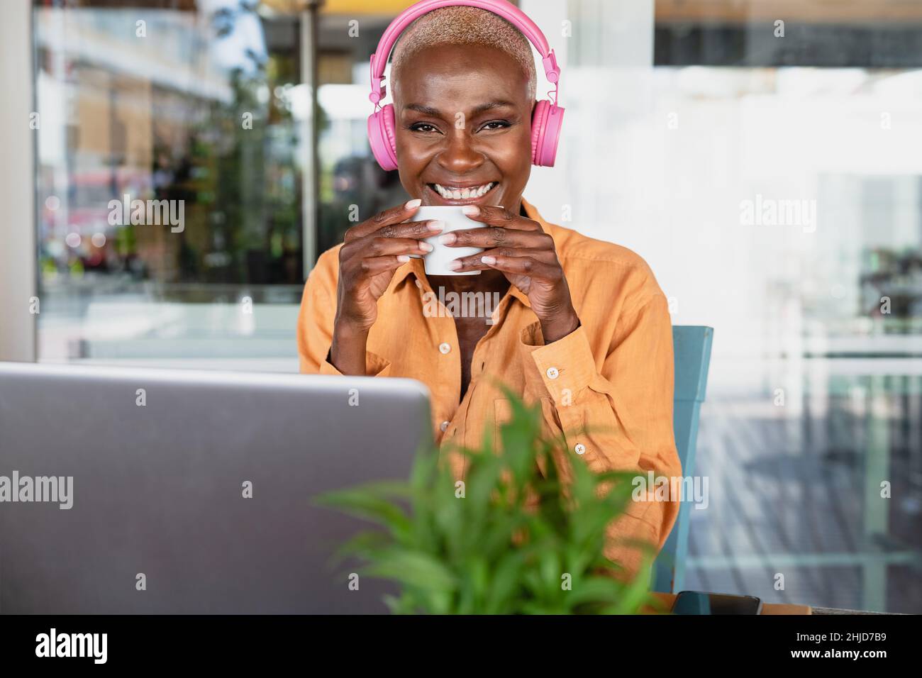 African woman drinking coffee while using laptop in coffee shop - Digital nomad and freelance lifestyle concept Stock Photo