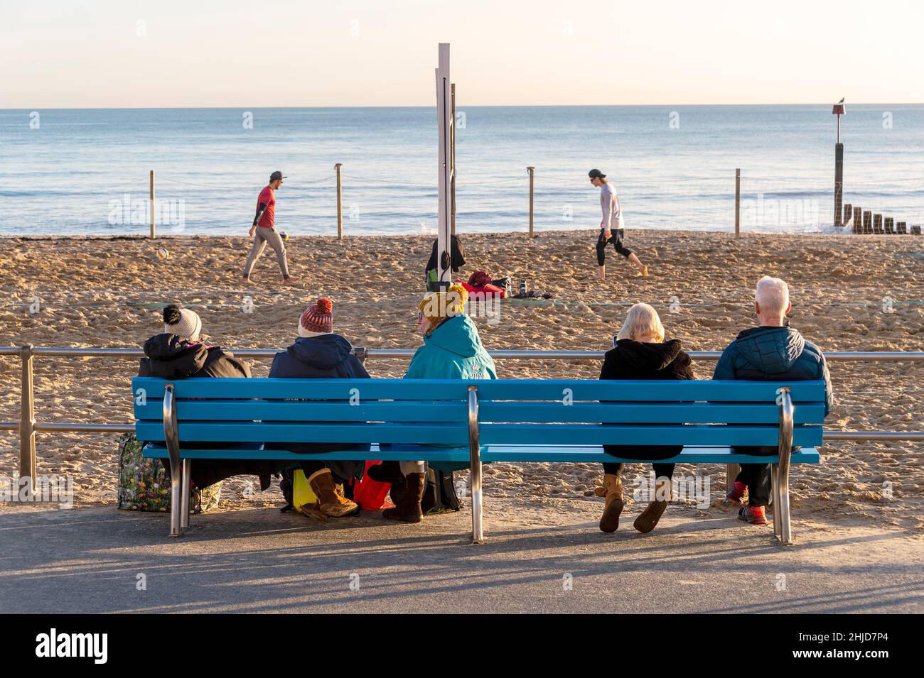 People sitting on a bench watching a game of beach vollyball Stock Photo