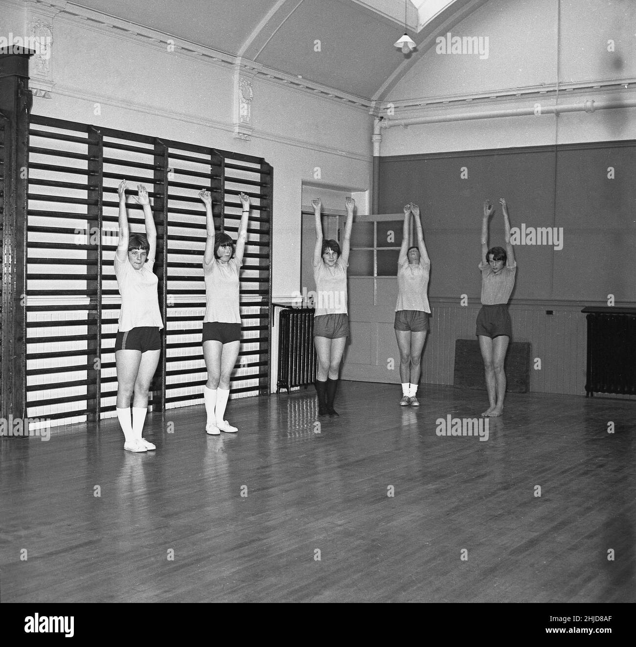 1960s, historical, youth club, inside a sports hall, ssome teenage girls in gym clothes, tops and shorts, and pumps, doing stretching exercises, Scotland, UK. In this era, much like the scouts and girl guides, local youth clubs played an important role in the community by providing young people with activities, both in and outdoors, that improved their health and self-esteem. Stock Photo