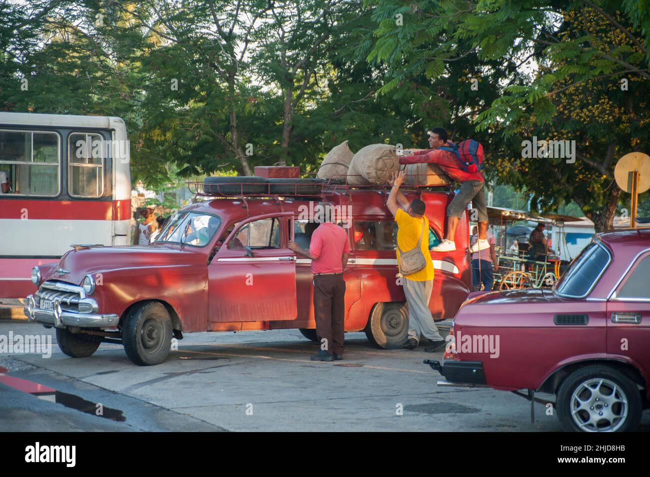 Cuban driver enters old taxi car with passengers while another man puts bags on top of the station wagon roof in Havana, Cuba. Stock Photo