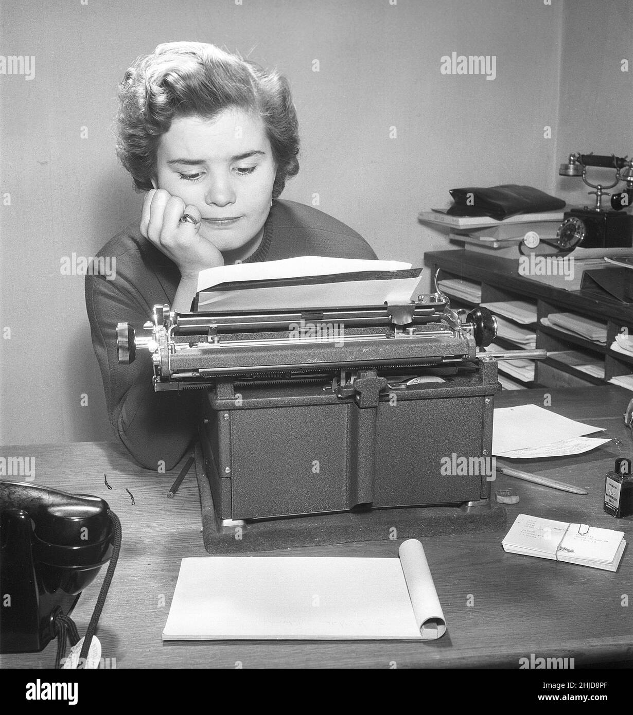 Office girl in the 1950s. A woman is sitting in front of her typewriter and looks att the text she has written. She is nicely dressed and gives a serious impression. Sweden 1954.Photo Kristoffersson BO24-8 Stock Photo