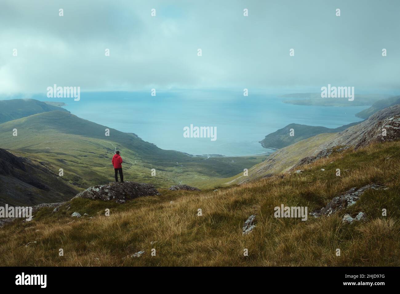A hiker at the top of the mountain views the magnificent landscape of the sea bay. Isle of Skye. Bla Bheinn, Isle of Skye, Scotland  Stock Photo