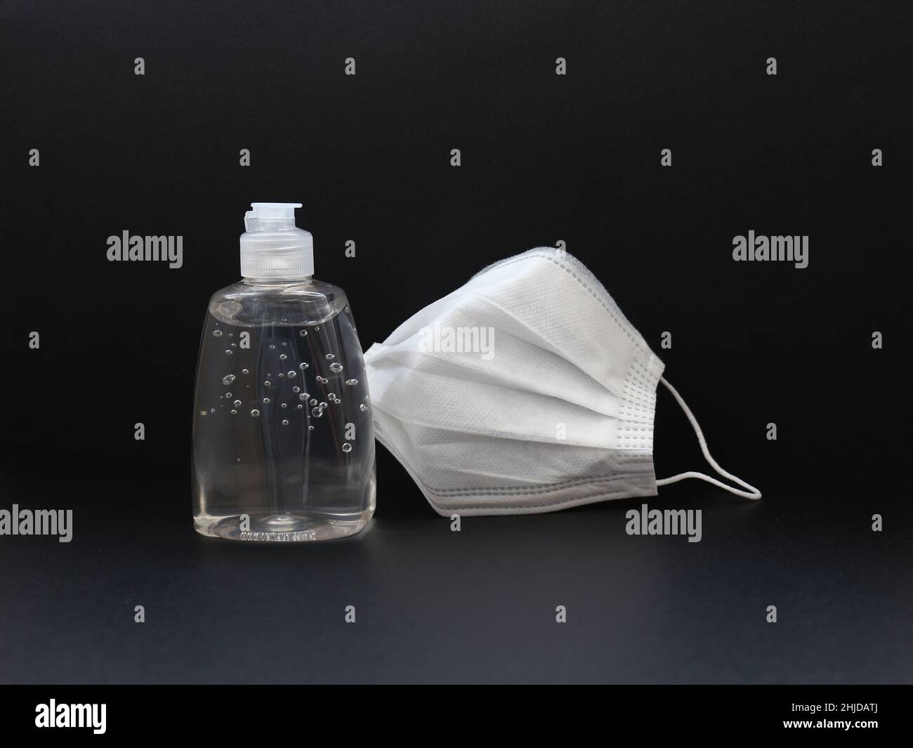 basic protective kit for covid19 pandemic, hand sanitizer gel in a transparent bottle and a white mask standing the closed bottle on black background Stock Photo