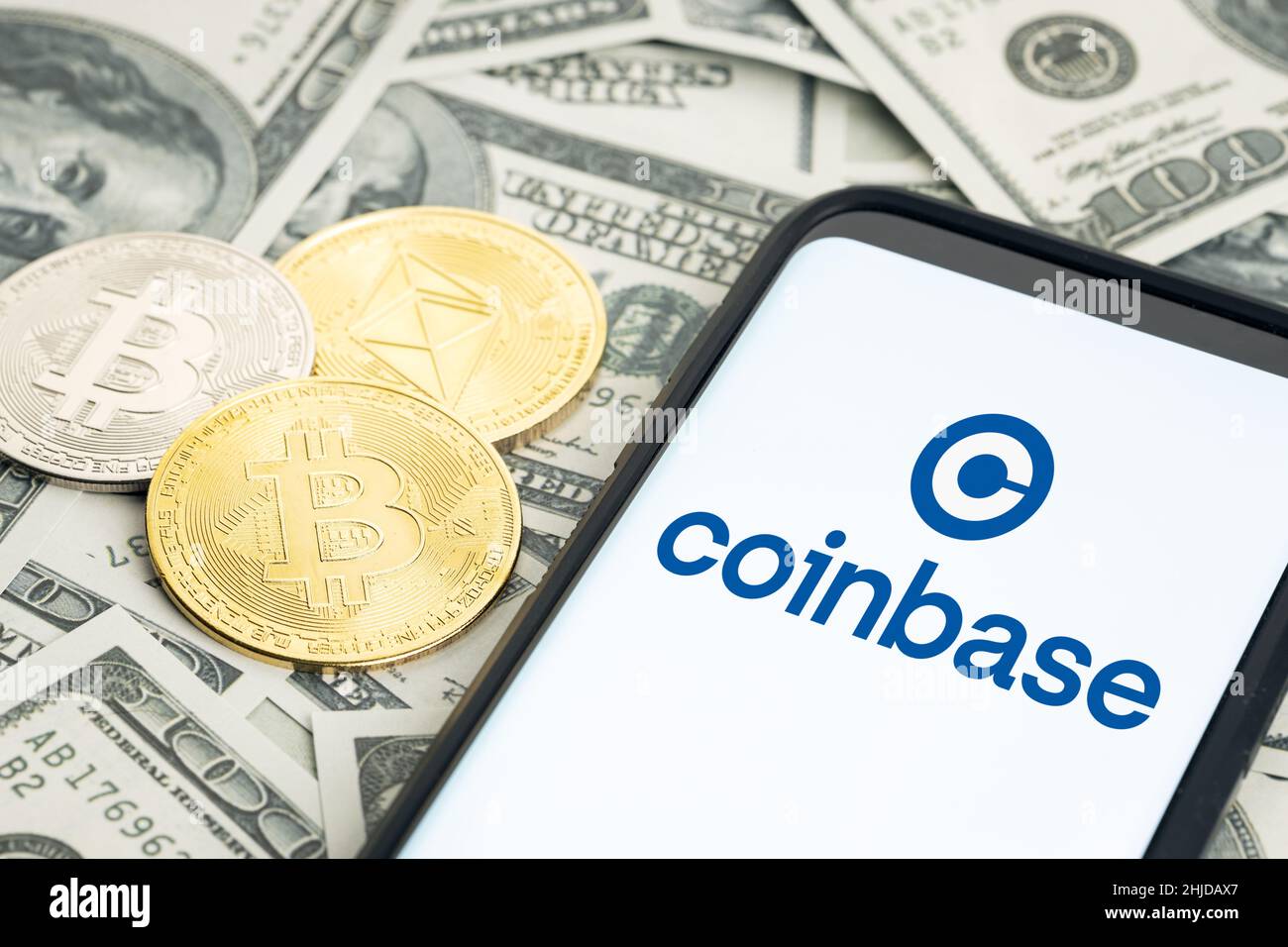 Galicia, Spain; january 28, 2022: Coinbase logo on Smartphone screen and dollar banknotes and bitcoin and ethereum coins Stock Photo