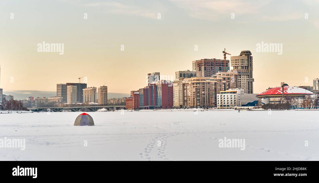 Winter cityscape of Yekaterinburg, Russia. Ice of city pond covered in snow, fisherman's tent. Stock Photo