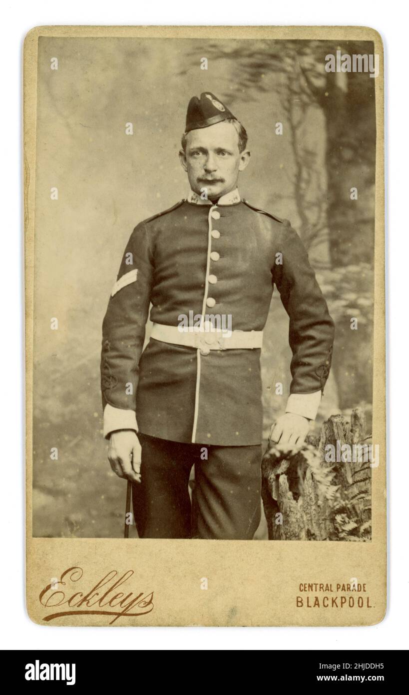 Original Victorian carte de viste (CDV) of soldier in ceremonial uniform in the East Lancashire regiment, (an infantry regiment) wearing a field service cap with a badge, holding a swagger stick, cuff braiding, the 2 chevrons on the sleeve denotes a corporal, In most units a corporal commands a section. From the studio of Eckleys, Blackpool, Lancashire, U.K. circa 1881. Stock Photo