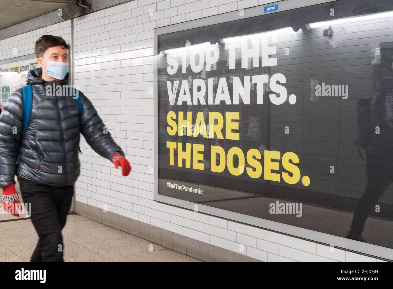 a man in face mask walks past huge poster on the billboard showing 'Stop the variants share the doses', London England UK Stock Photo
