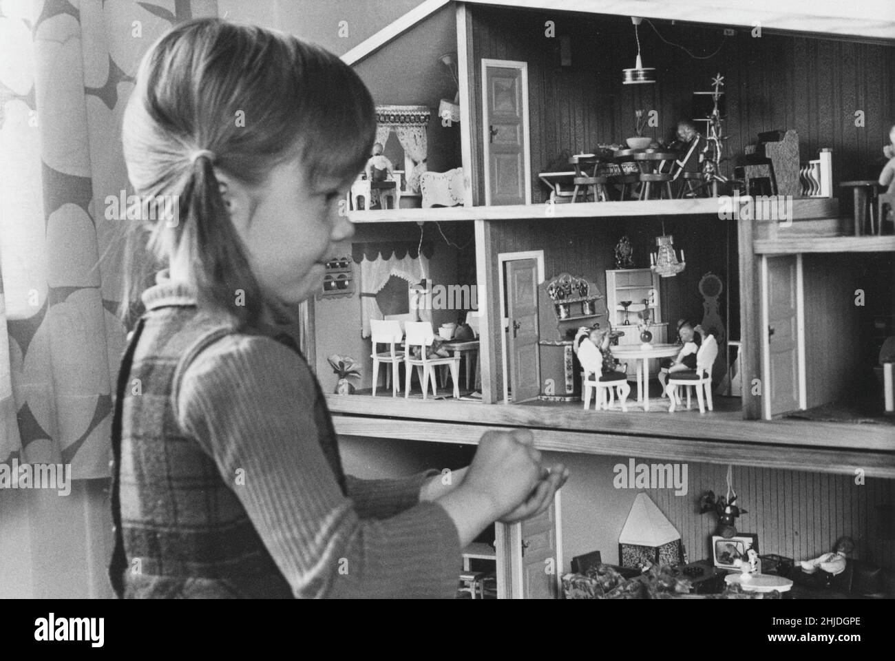 Playing in the 1970s. A little girl is playing with her dolls house that is decorated with nice furniture and dolls. Sweden 1973 Stock Photo