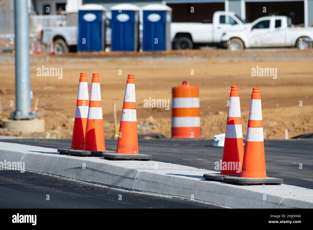 Horizontal shot of a group of orange traffic cones in front new apartment construction.  Three porta potties in the background. Stock Photo