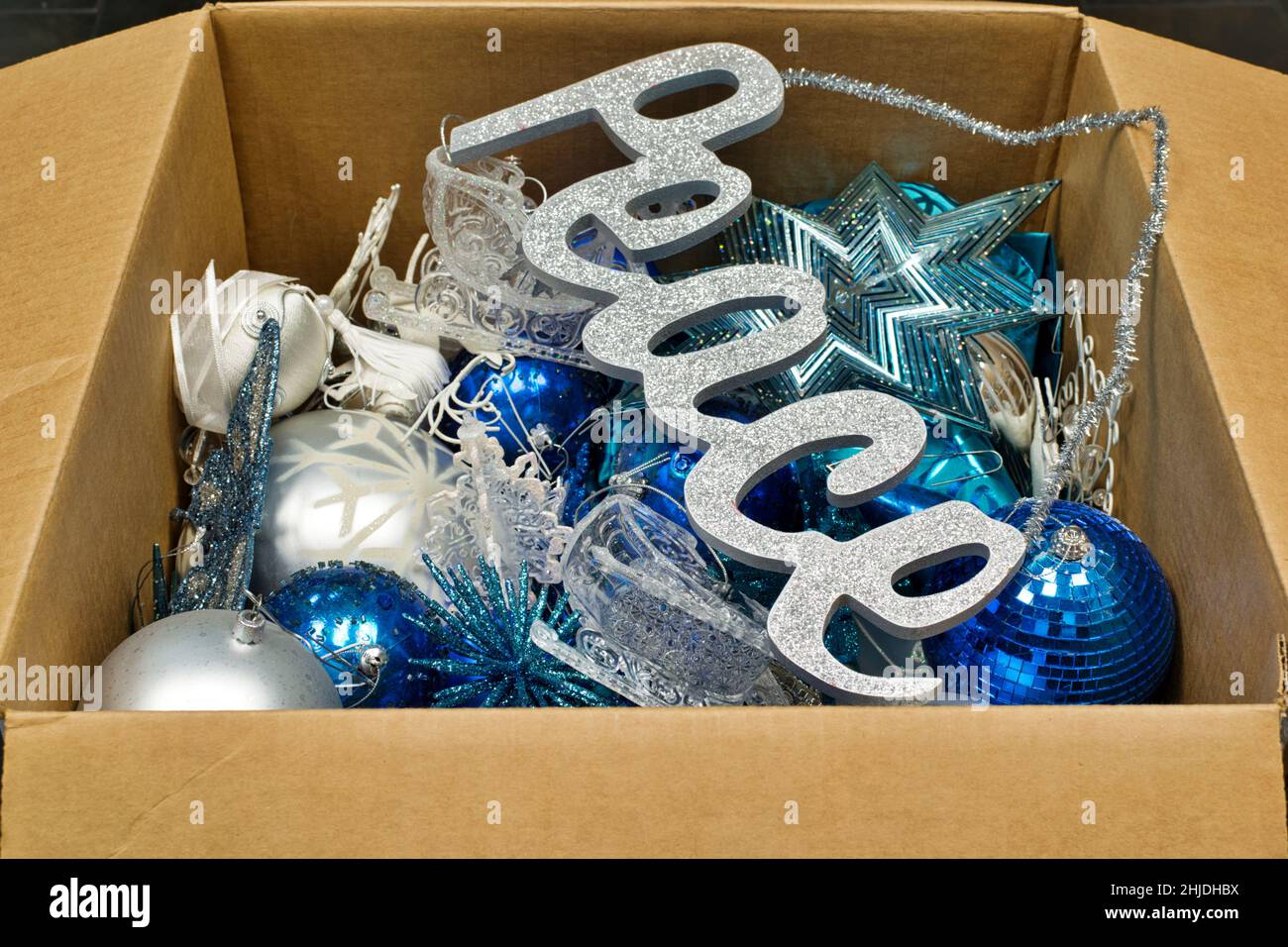 Christmas ornaments and a peace sign decoration in an open cardboard box packed away after the new year, low angle view. Stock Photo