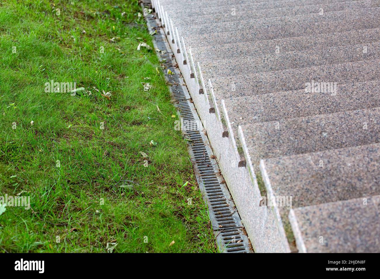 Drainage system on a slope with green grass and iron rainfall system near a granite stairs with stone steps close-up, nobody. Stock Photo