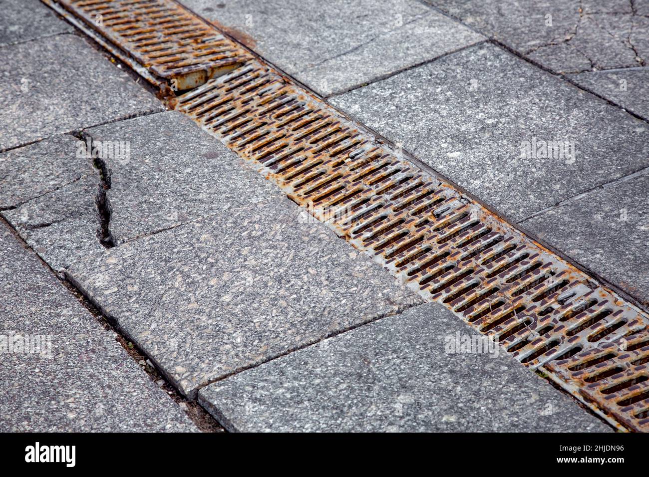 old rusty drainage grate on granite pavement with ruined cracked tiles