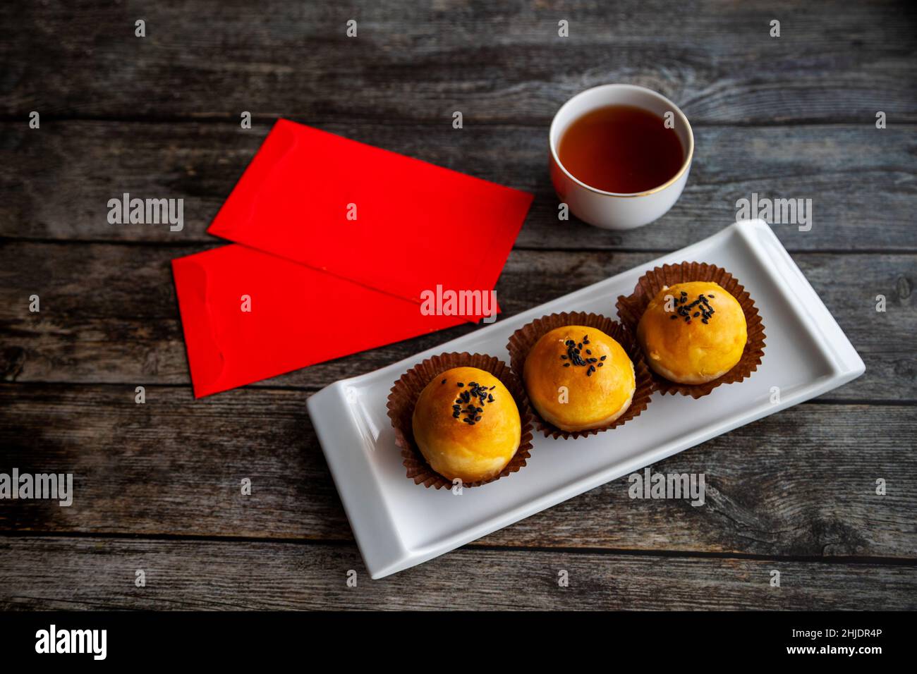 Traditional Chinese New Year pastries baked with fluffy dough and filled with salted egg yolk and sweet paste. Chinese lucky money red packets and tea Stock Photo