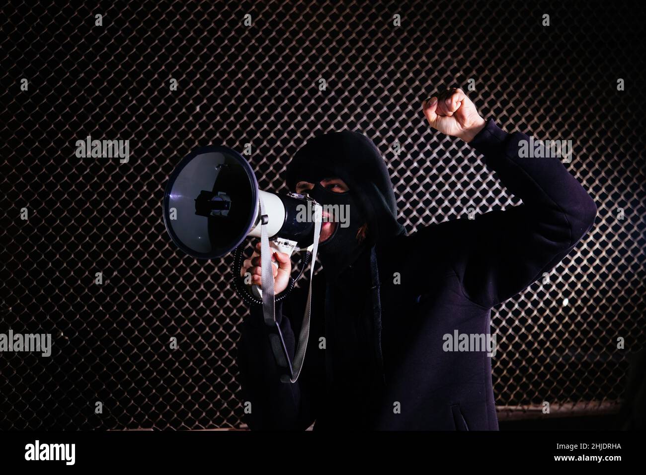Angry masked man is shouting into the megaphone. Stock Photo