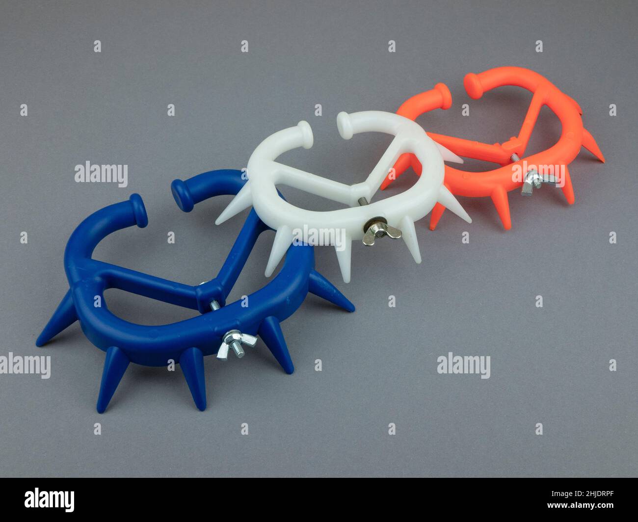 Different sized weaning rings that prevent calves from sucking. Calf weaning ring of bright orange, blue and white plastic on the gray background Stock Photo
