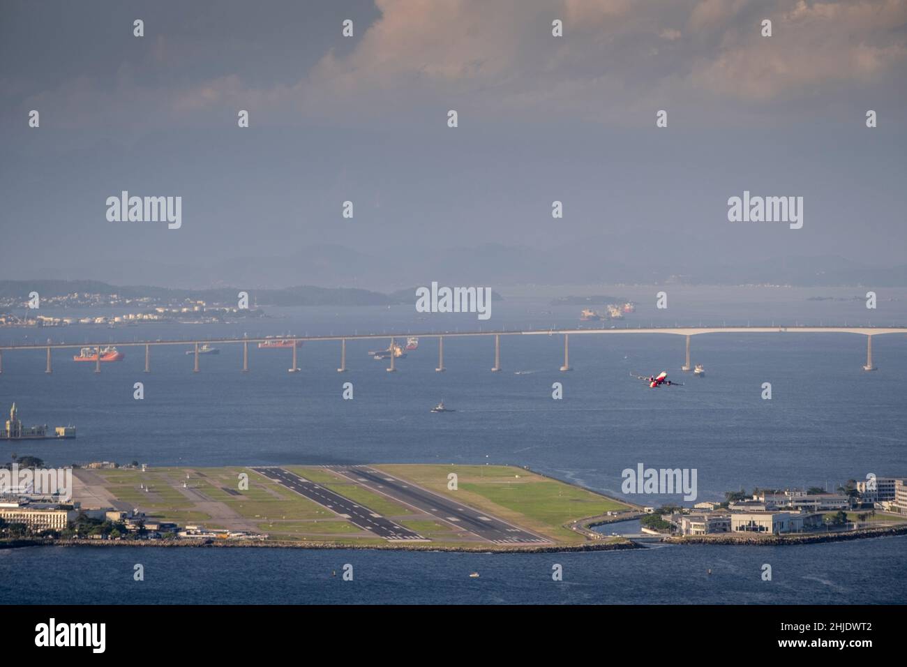 Brazil, Rio de Janeiro. Plane taking off from runway at Santos Dumont airport in city centre. Guanabara Bay & Rio-Niteroi bridge behind. Daytime. Stock Photo