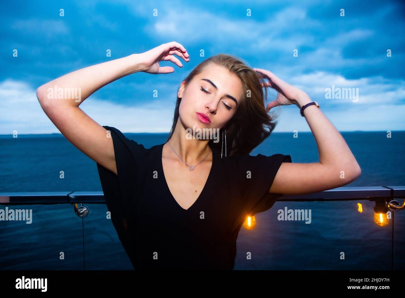 Young Ukrainian lady enjoys her time in a night club in Odessa on the shore of the Black Sea in romantic mood. A drama sky adds contrast to her image. Stock Photo