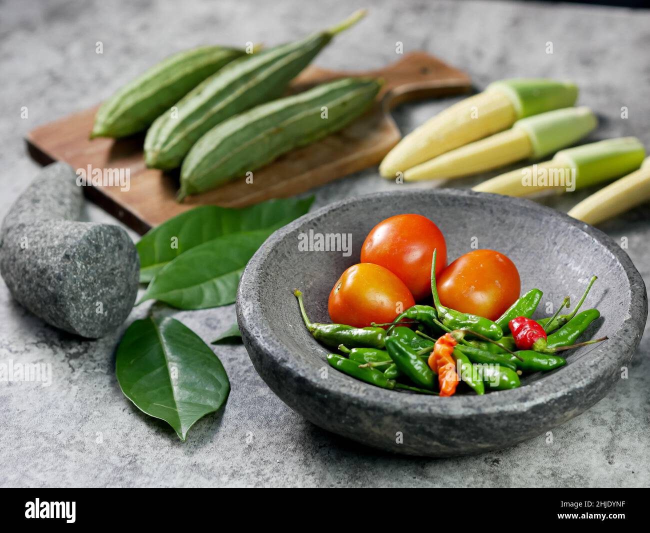 chilies and tomatoes in a mortar, recipe for vegetable baby corn and luffa acutangula with tomato sauce. food preparation concept. Stock Photo