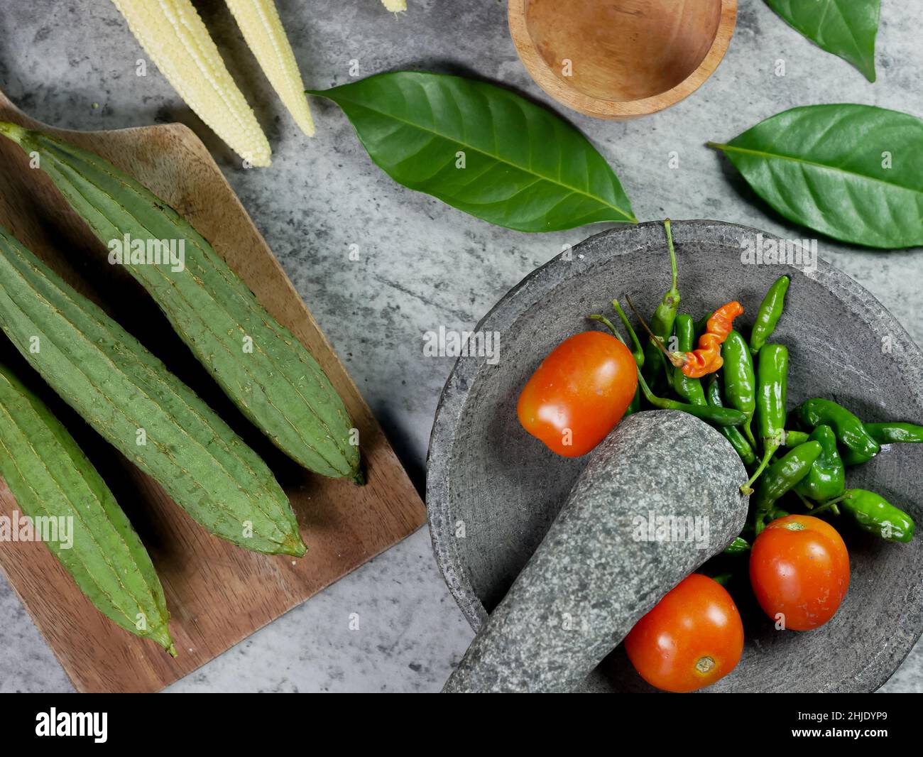 chilies and tomatoes in a mortar, recipe for vegetable baby corn and luffa acutangula with tomato sauce. food preparation concept. top view Stock Photo
