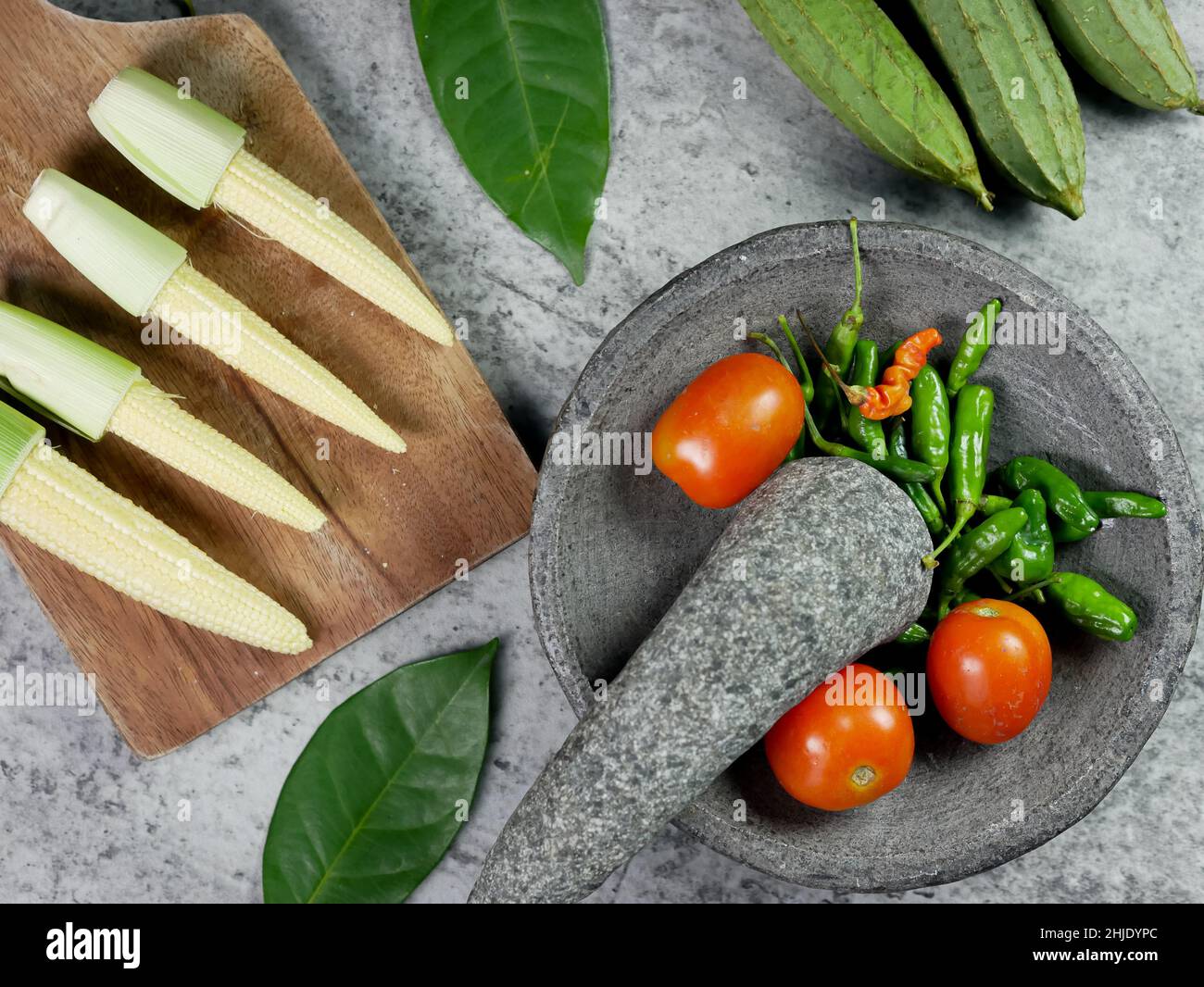 chilies and tomatoes in a mortar, recipe for vegetable baby corn and luffa acutangula with tomato sauce. food preparation concept. top view Stock Photo