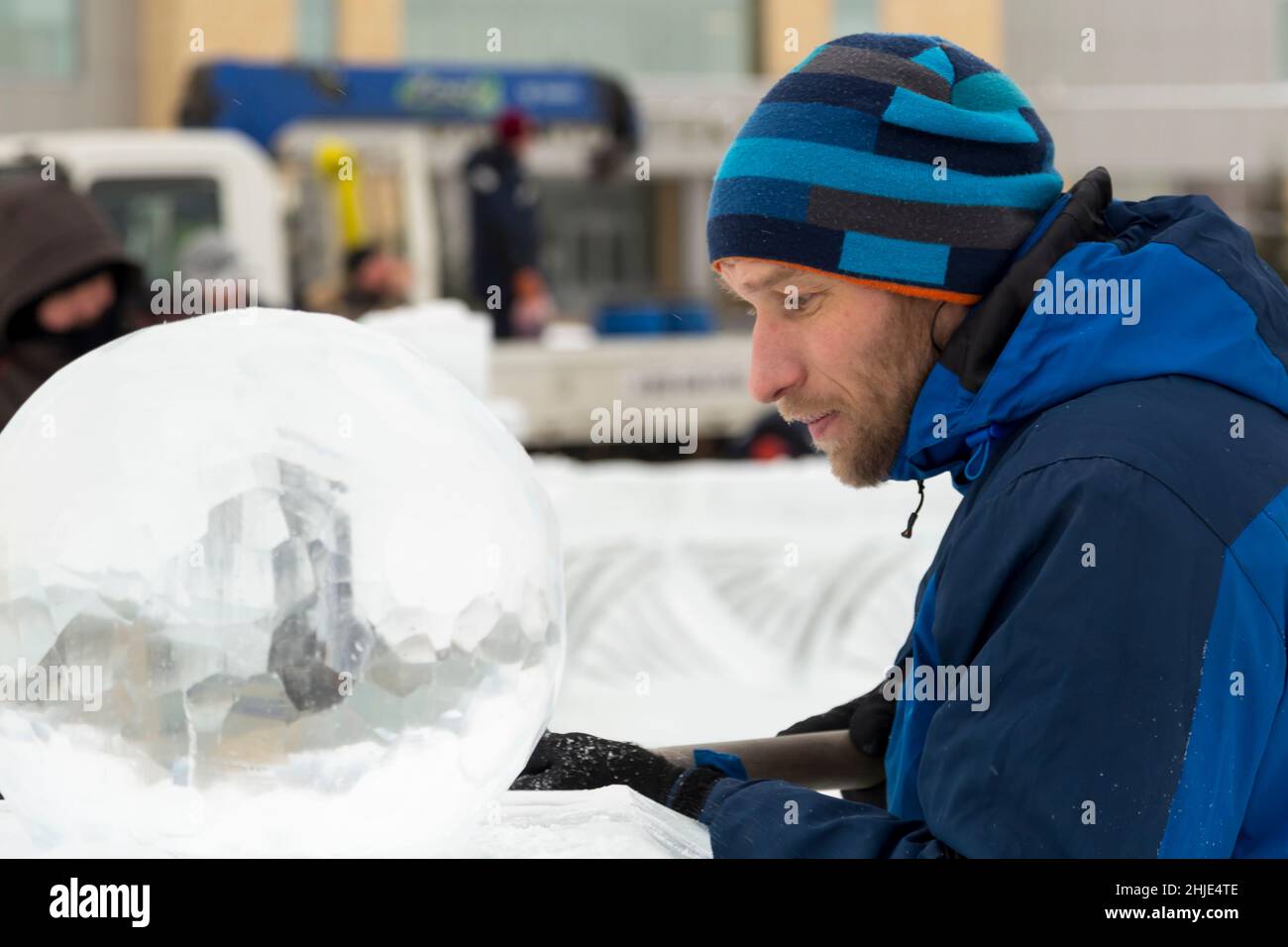 A sculptor carves a round ice ball out of a block of ice with a chisel ...