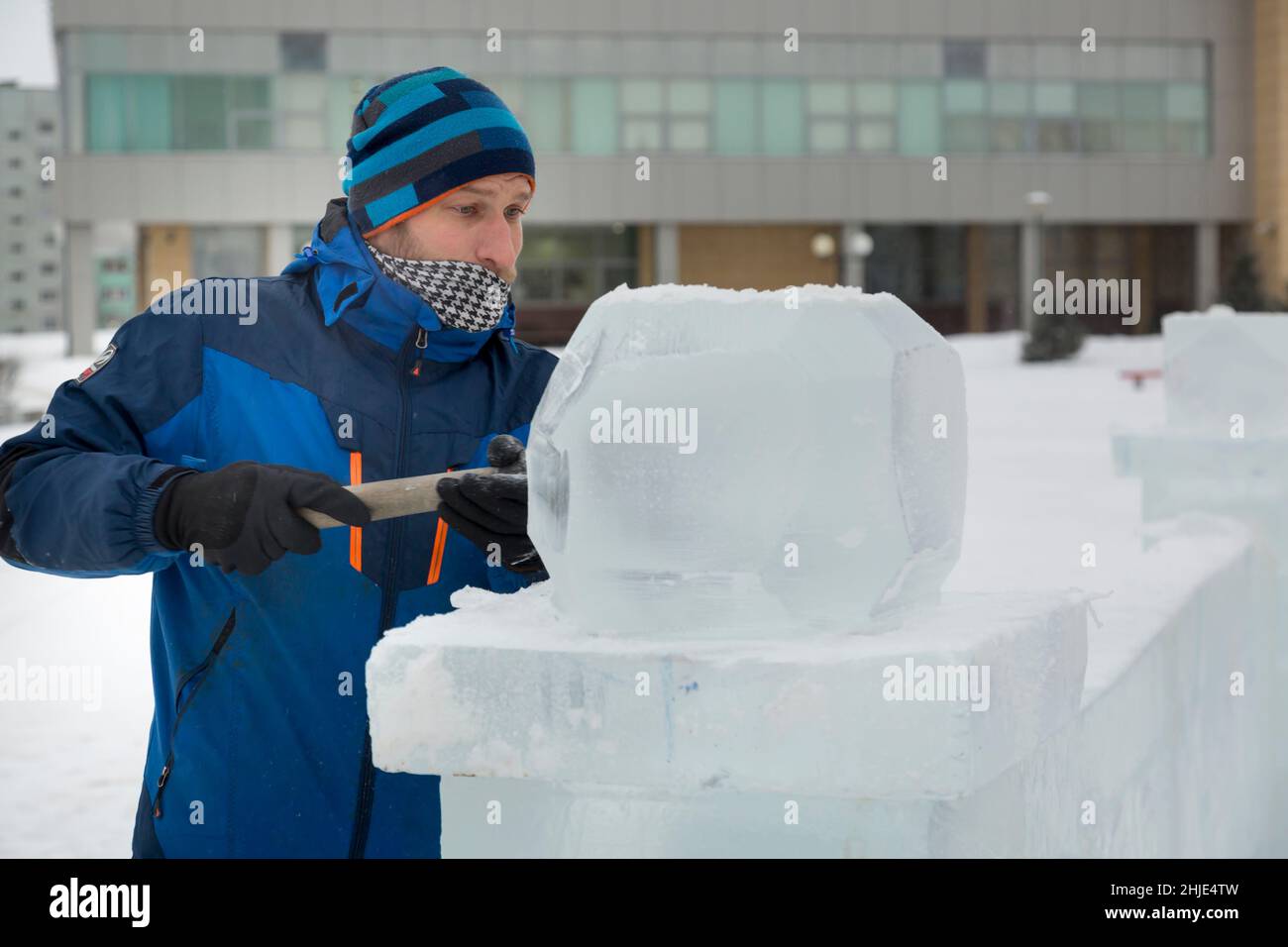 A sculptor carves a round ice ball out of a block of ice with a chisel ...