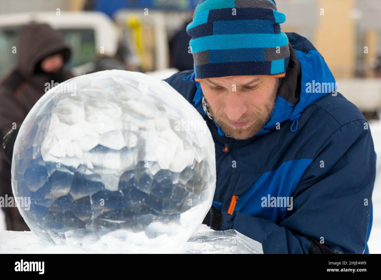 A sculptor carves a round ice ball out of a block of ice with a chisel ...