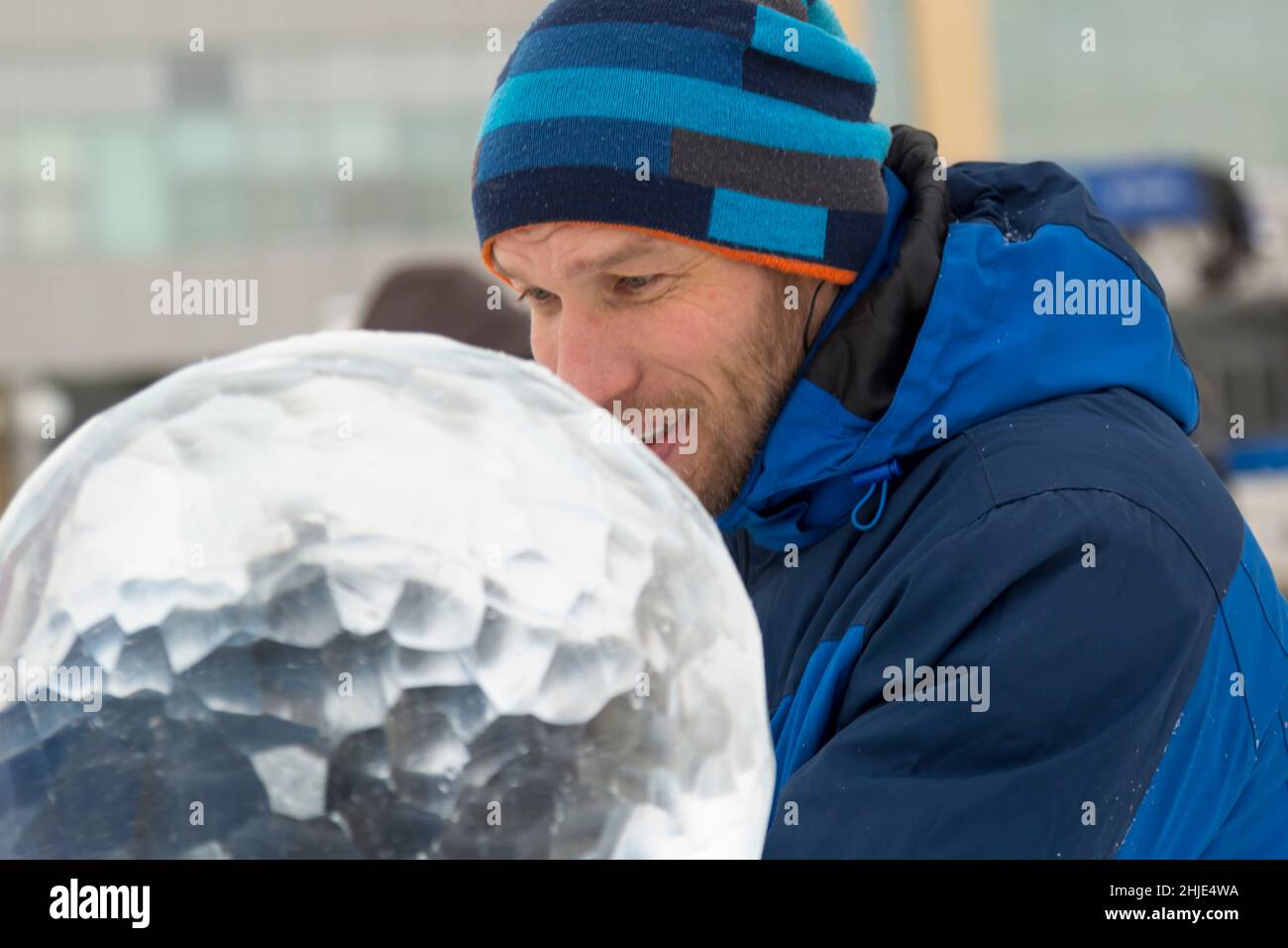 A sculptor carves a round ice ball out of a block of ice with a chisel ...