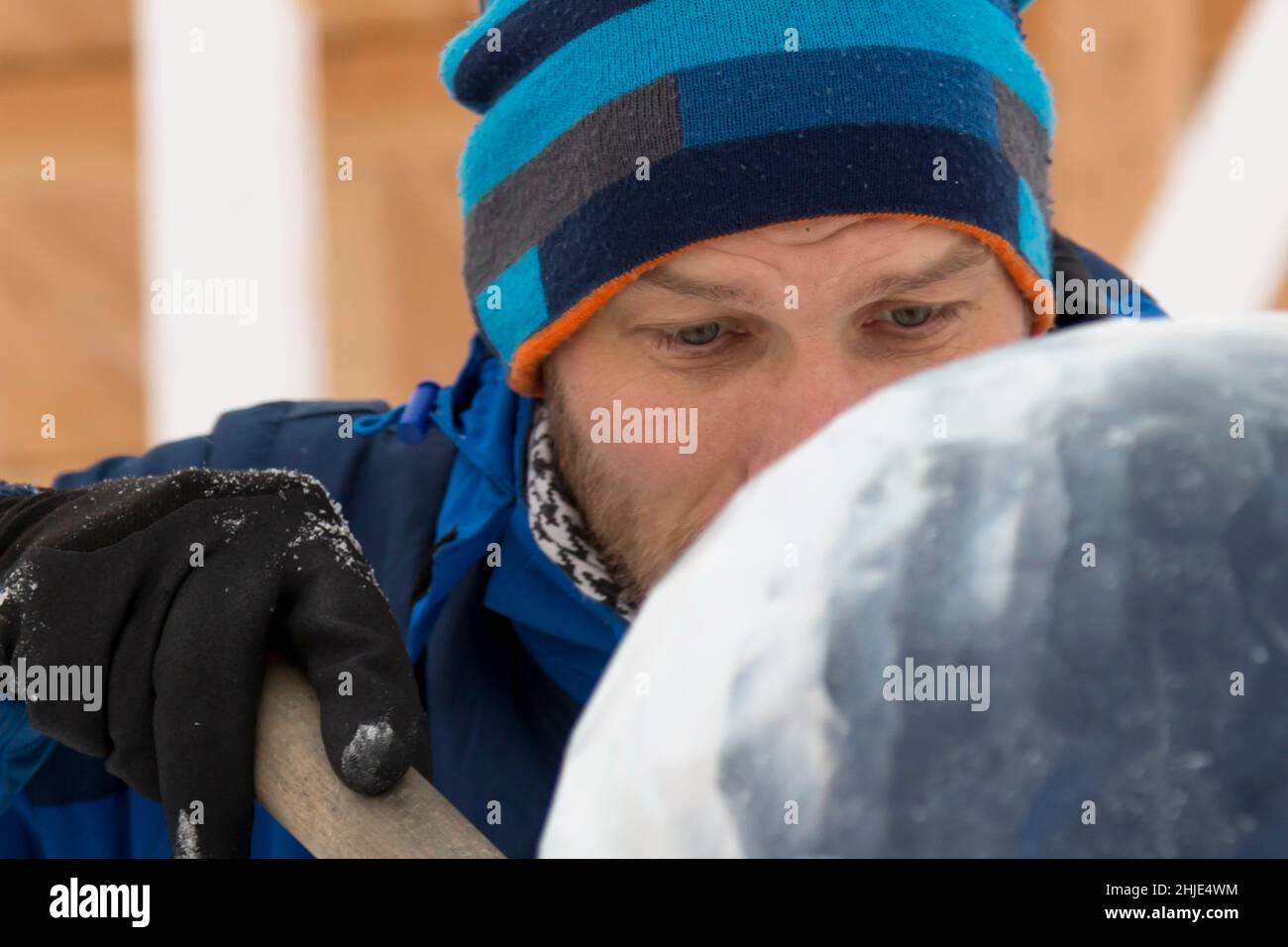 A sculptor carves a round ice ball out of a block of ice with a chisel ...