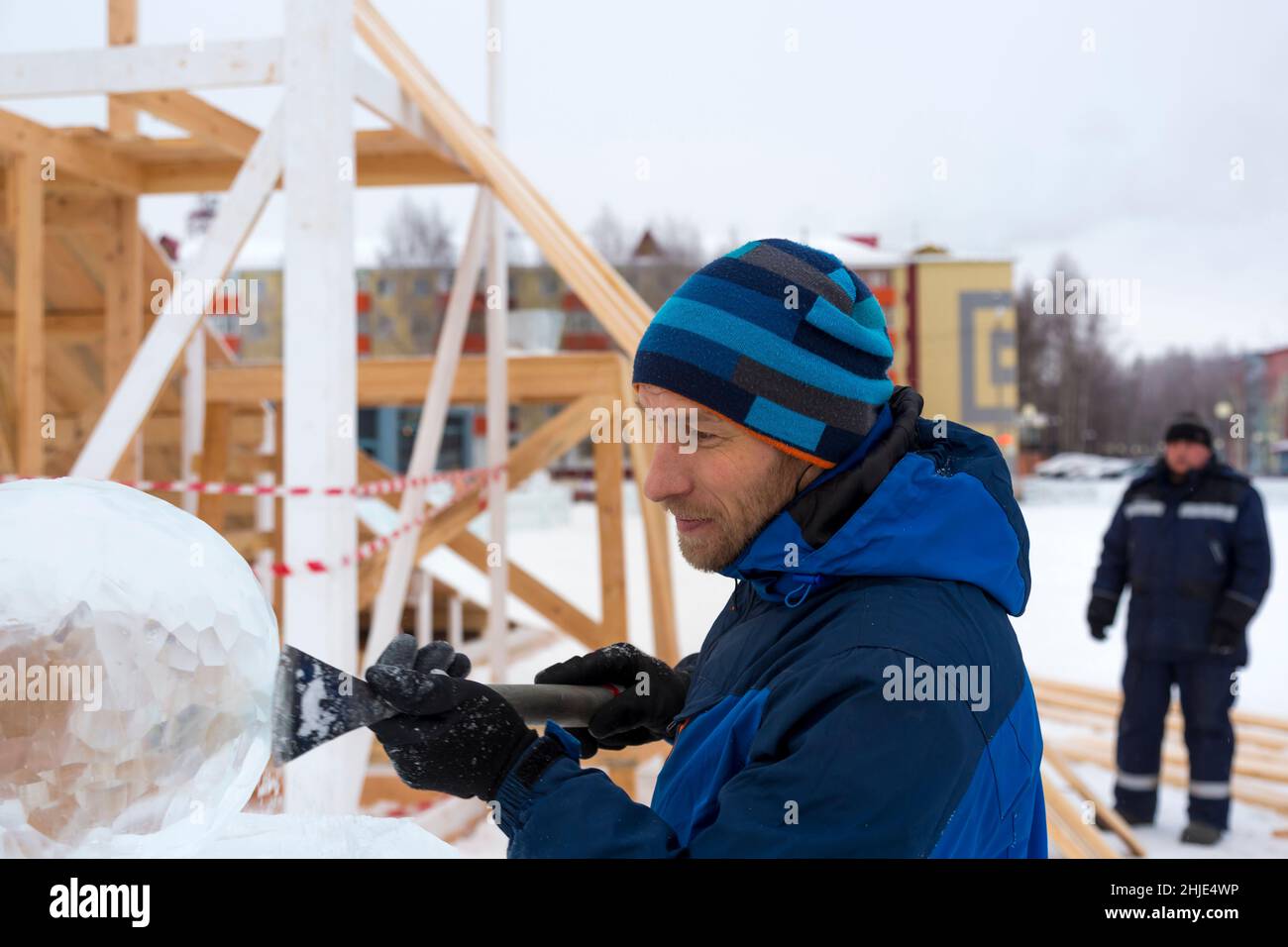 A sculptor carves a round ice ball out of a block of ice with a chisel ...