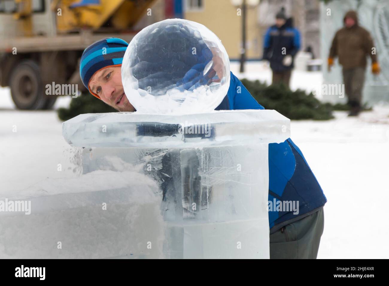 A sculptor carves a round ice ball out of a block of ice with a chisel ...