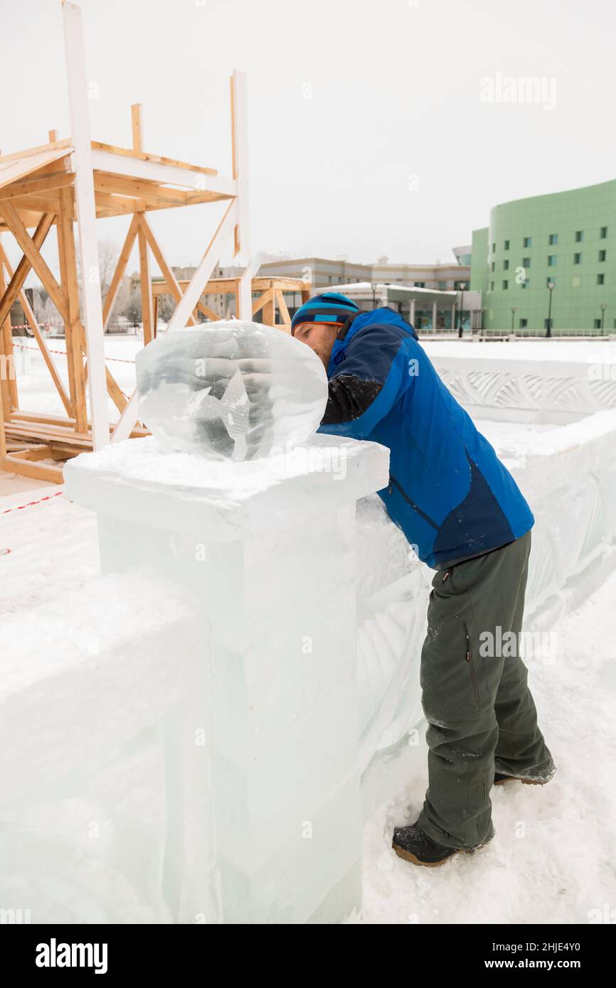 A sculptor carves a round ice ball out of a block of ice with a chisel ...