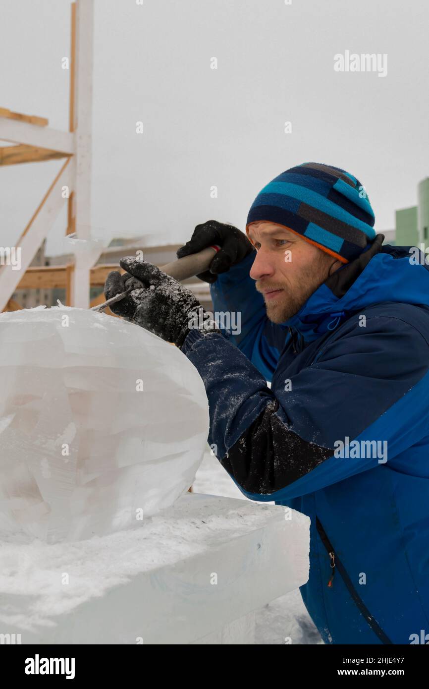 A sculptor carves a round ice ball out of a block of ice with a chisel ...