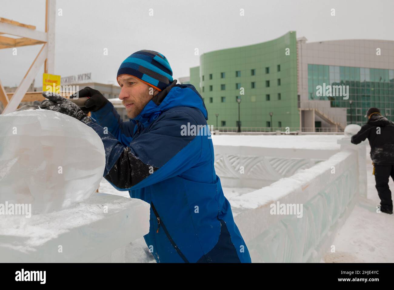 A sculptor carves a round ice ball out of a block of ice with a chisel ...