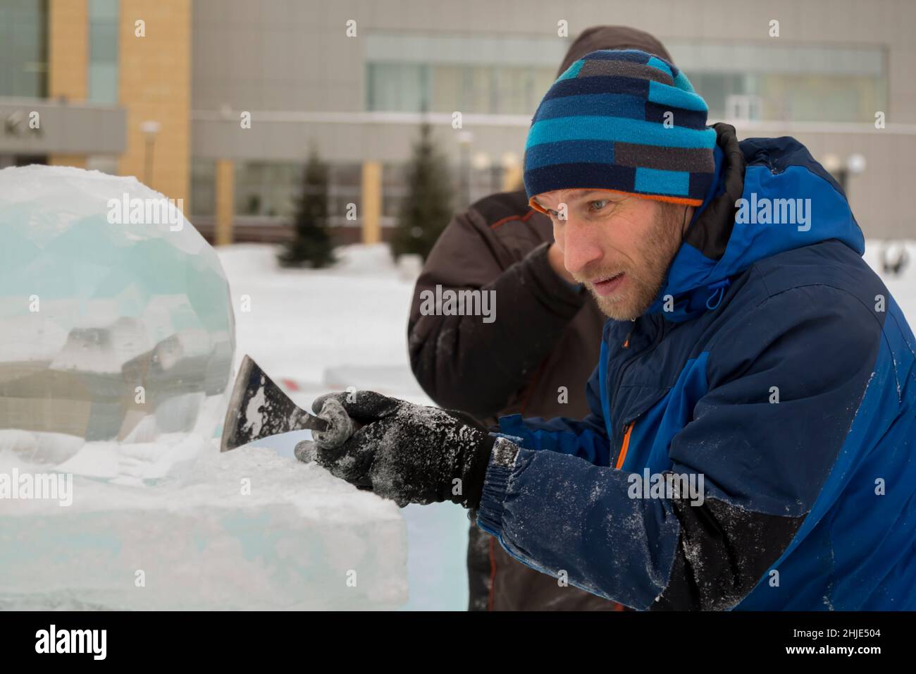 A sculptor carves a round ice ball out of a block of ice with a chisel ...