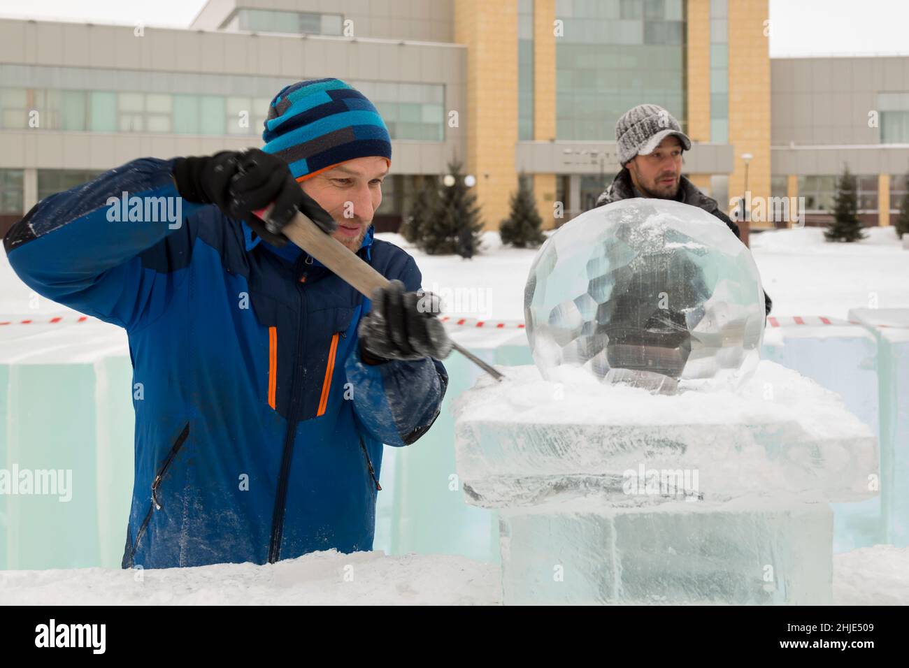 A sculptor carves a round ice ball out of a block of ice with a chisel ...