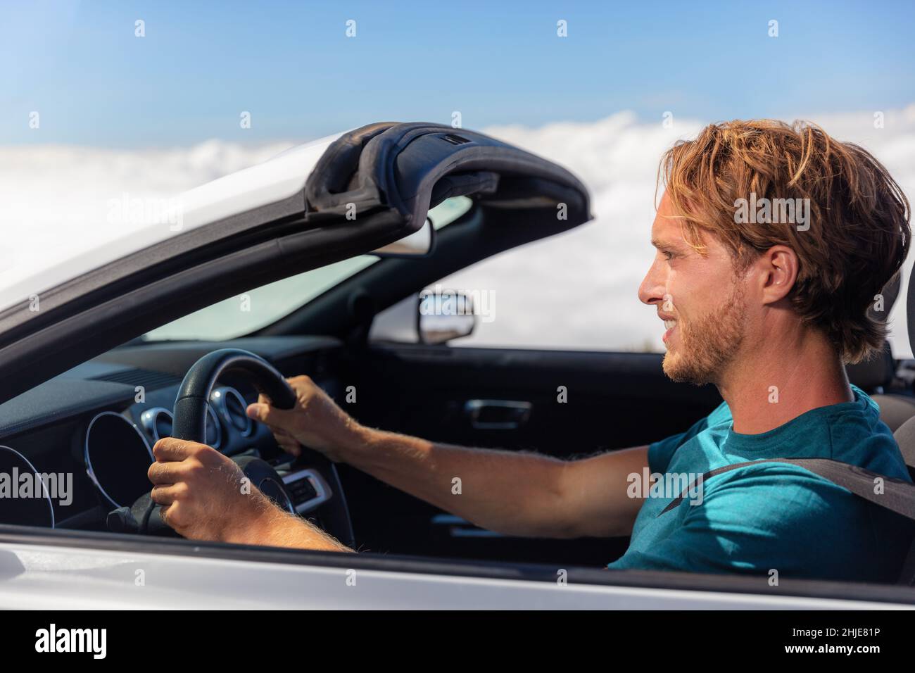 Road trip drive young man driver driving open roof convertible sports car on summer travel holiday vacation. Side profile portrait youn guy in his 30s Stock Photo