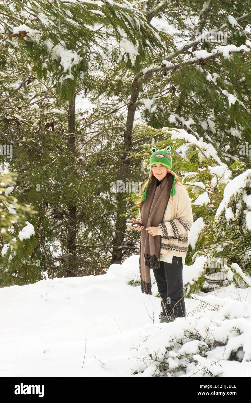 Mevasseret Zion, Israel - January 27th, 2022: A teenage girl standing in a snowy forest, holding her smart phone and smiling to the camera. Stock Photo