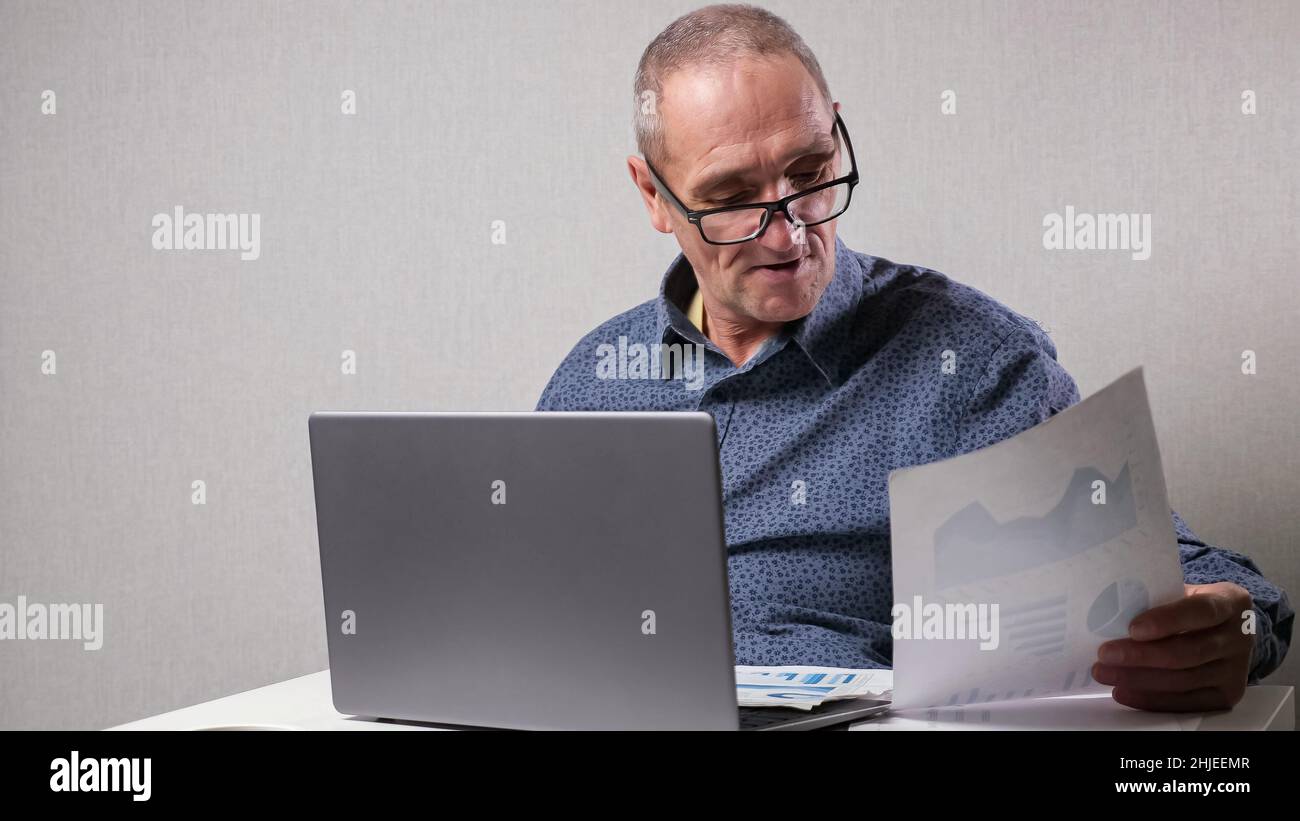 Senior man sits near computer checking reports in office Stock Photo