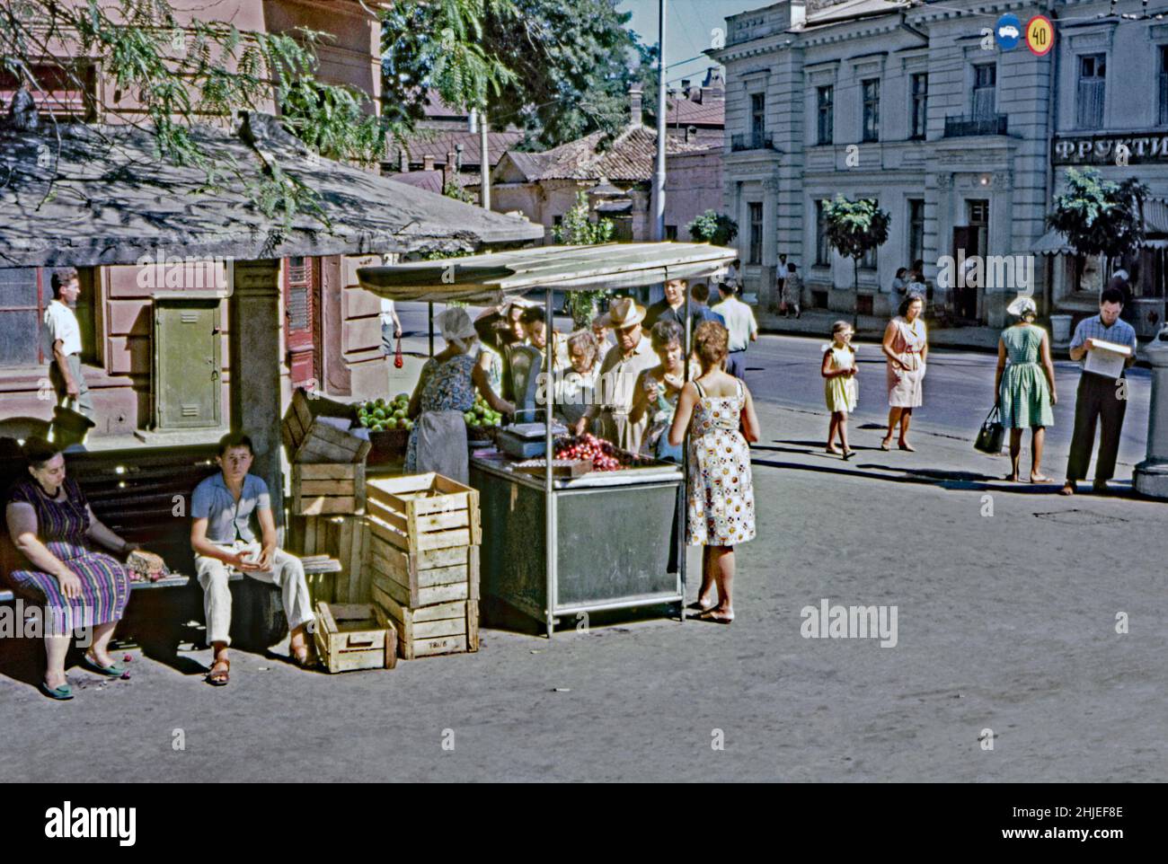 A 1960s photograph of a female street trader selling fruit and vegetables from a roadside undercover stall in the summer sunshine in Moscow, Russia. Often market gardeners and owners of smallholdings from outside the city would come into town each week to sell their home-grown produce. Here it looks like plums and apples are the main attraction for the queue of shoppers. This image is from an amateur Agfacolor 35mm colour transparency – a vintage 1960s photograph. Stock Photo