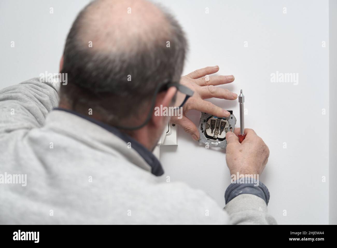Senior electrician installing new current socket with screwdriver. Stock Photo