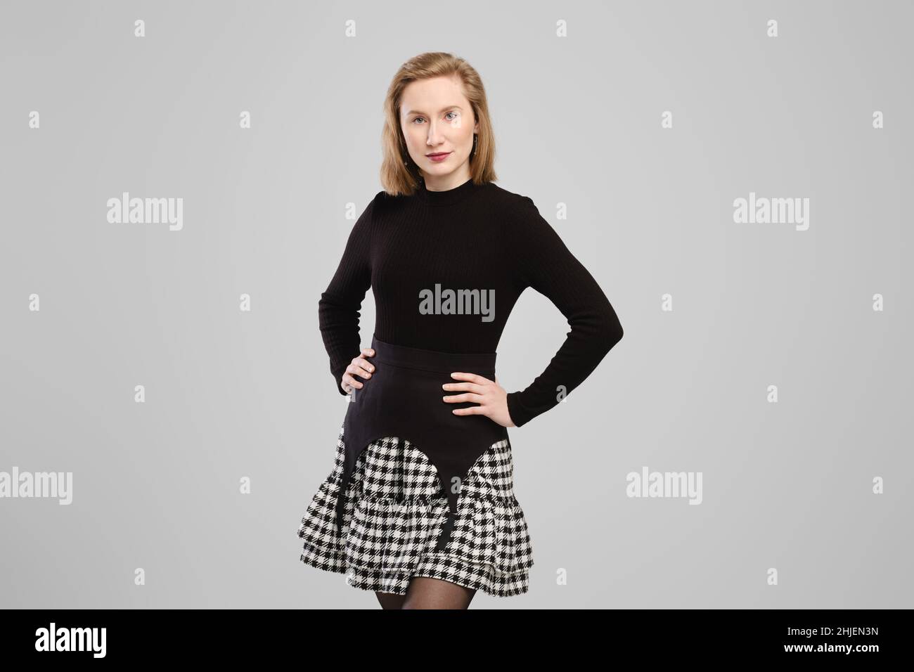 Young woman in turtleneck and suspender belt over little skirt posing in studio over grey background Stock Photo